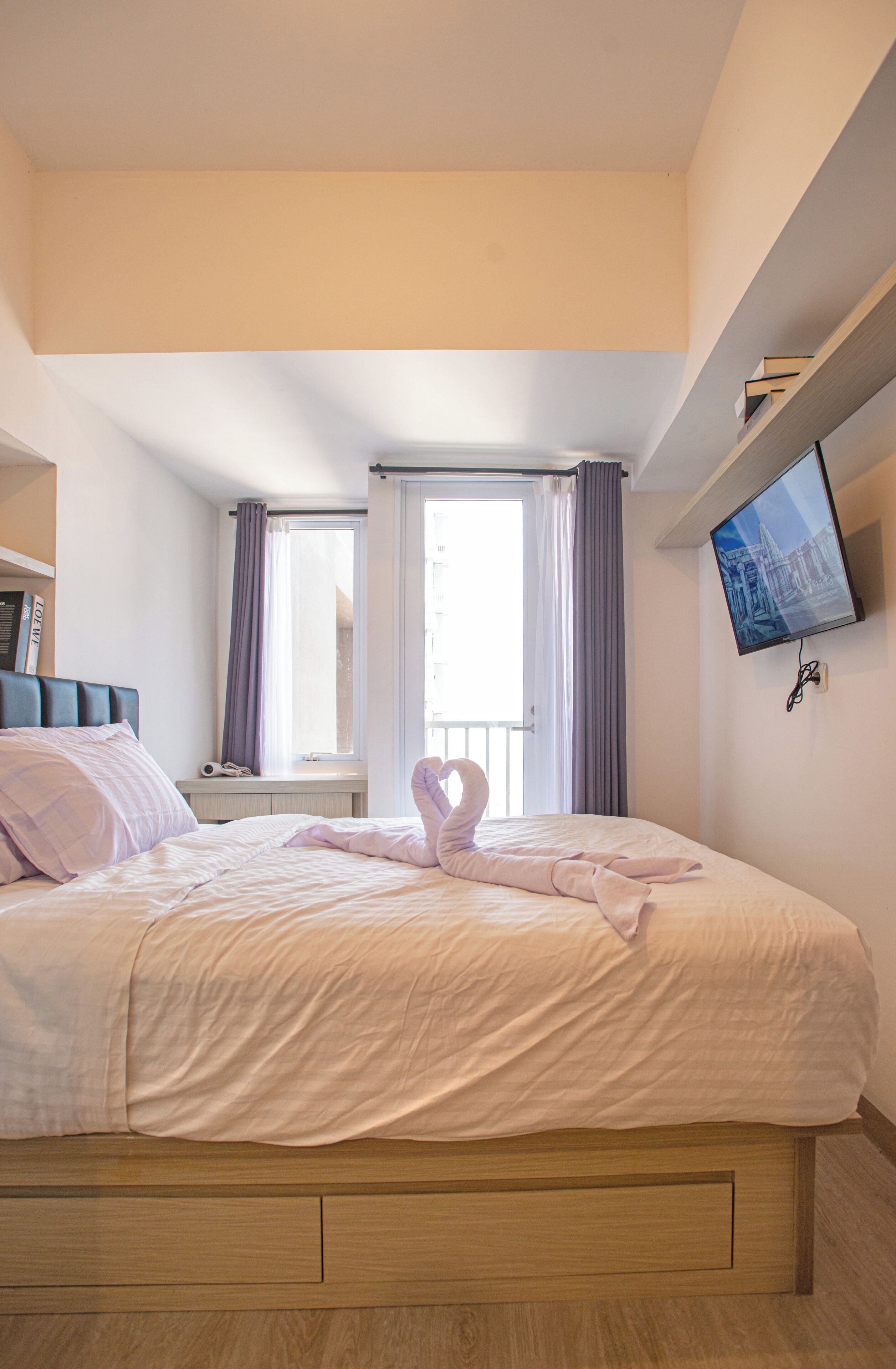 A bedroom with a bed, a television mounted on the wall, and a window with curtains.
