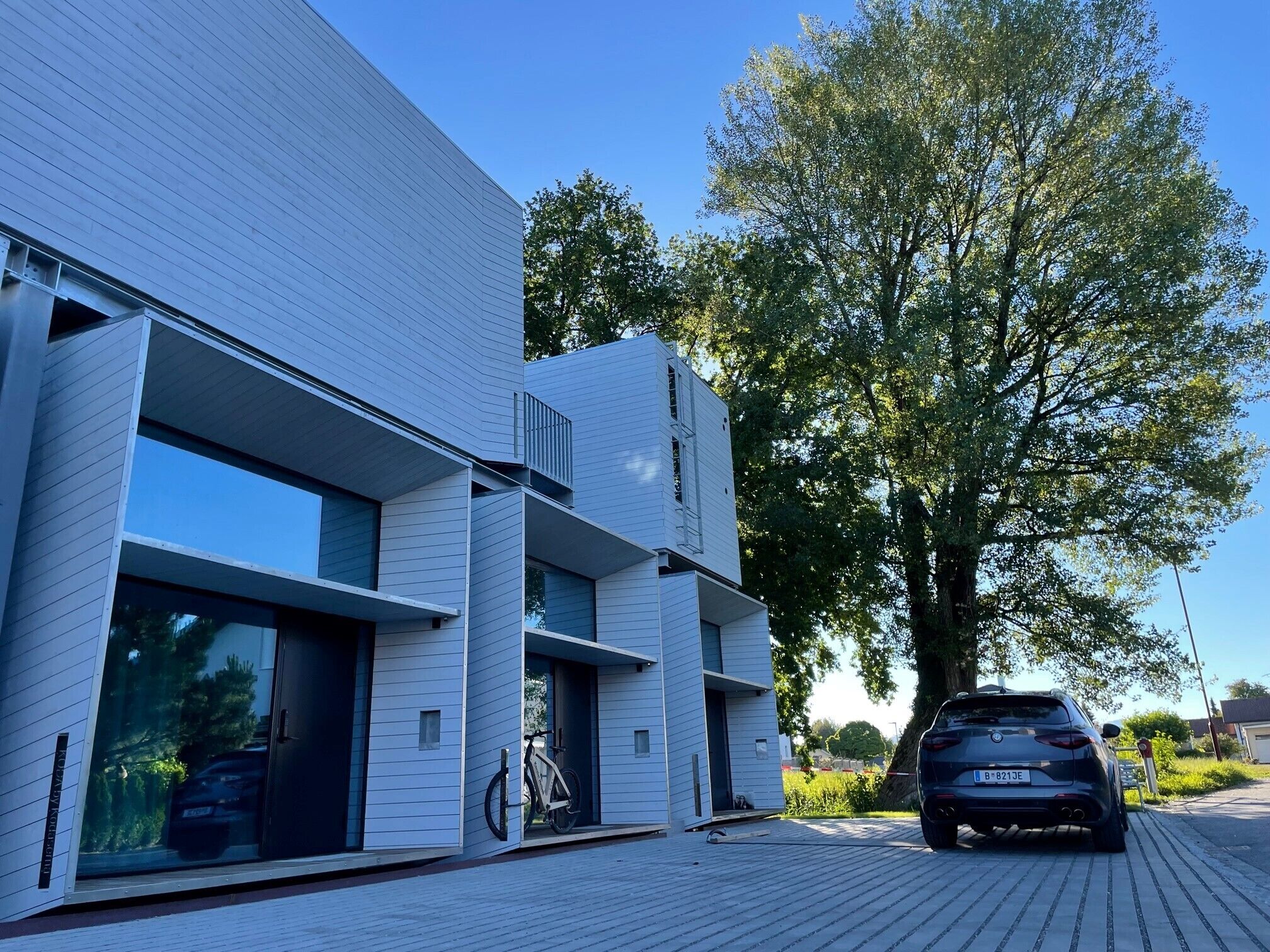 A modern two-story building with large windows and a car parked in the driveway.