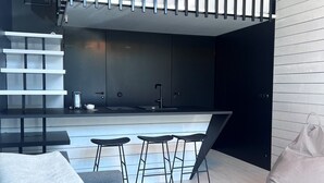 Un interior moderno con cocina, zona de comedor con taburetes, sofá y sillón de saco.