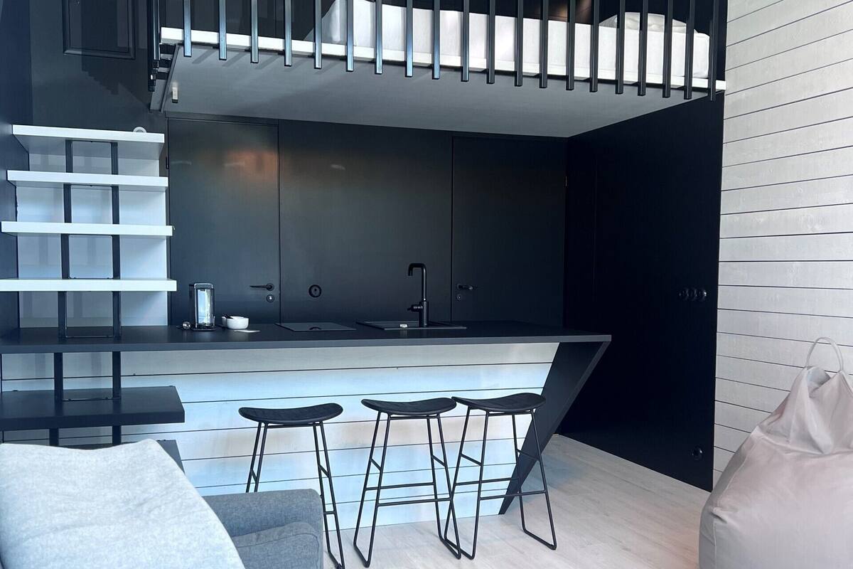 Een modern interieur met een keukenhoek, een zithoek met krukjes, een bank en een relaxfauteuil.
