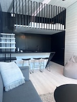 Un interior moderno con cocina, zona de comedor con taburetes, sofá y sillón de saco.