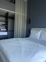 Una habitación de hotel moderna con una cama grande, un armario empotrado y una lámpara colgante.