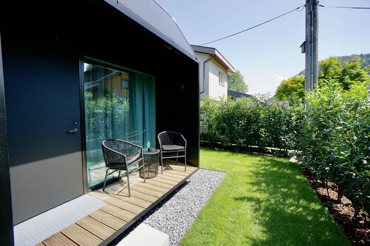 Een modern huis met een glazen deur naar een terras met twee stoelen en een tafel.