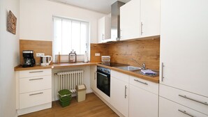 Eine kleine Küche mit weißen Schränken, einer Holz Arbeitsplatte, einem eingebauten Ofen und einem Fenster.