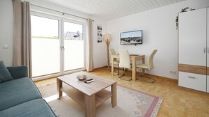 Ein modernes Wohnzimmer mit einer Couch, einem Holztisch, einem Esstisch mit Stühlen und einem an der Wand befestigten Fernseher.