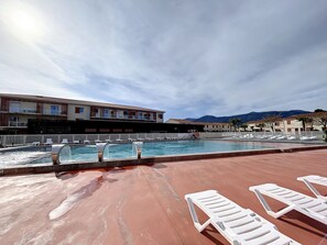 A pool area with lounge chairs, a building with balconies, and mountains in the background. - Apartment T2 with private terrace in Argelès-sur-Mer (Argelès-sur-Mer)