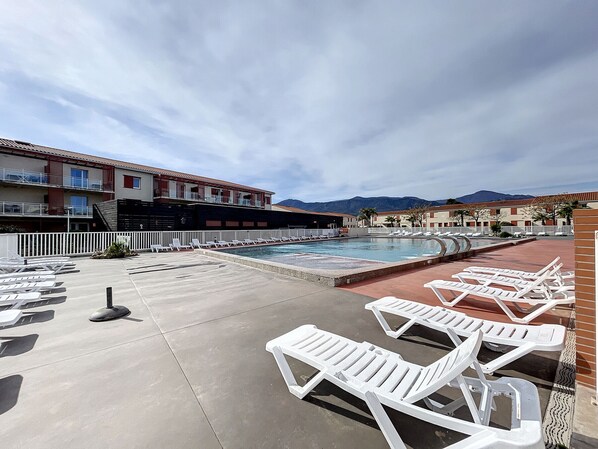 A pool area with white lounge chairs, a pool, and buildings in the background. - Apartment T2 with private terrace in Argelès-sur-Mer (Argelès-sur-Mer)
