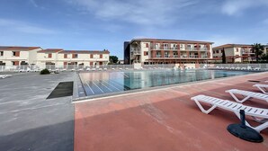 Ett poolområde på taket med solstolar, en swimmingpool och en byggnad med flera balkonger i bakgrunden.