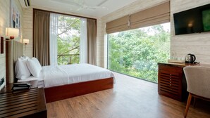 Een moderne hotelkamer met een groot bed, een bureau met stoel, een televisie en een balkon met uitzicht op bomen.