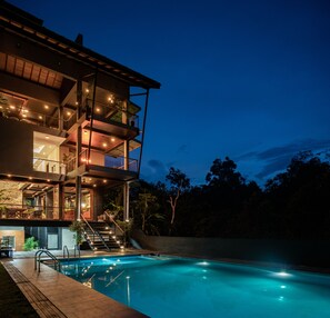 Um edifício com vários andares, piscina, área de estar externa e escadaria que leva aos níveis superiores.
