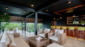 Een moderne lounge met rieten meubels, een glazen bijzettafeltje en een bar voorzien van flessen.