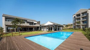 A modern hotel with a swimming pool, outdoor seating, and a well-maintained garden.
