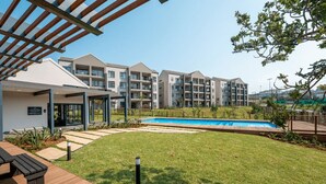 A modern residential building with a swimming pool, outdoor seating, and a well-maintained lawn.
