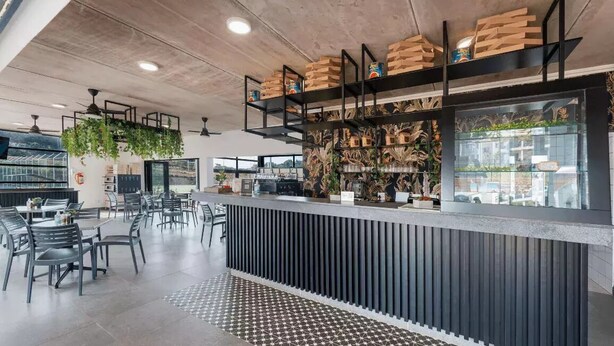 A modern bar area with a counter, shelves with boxes, hanging plants, and a patterned floor.