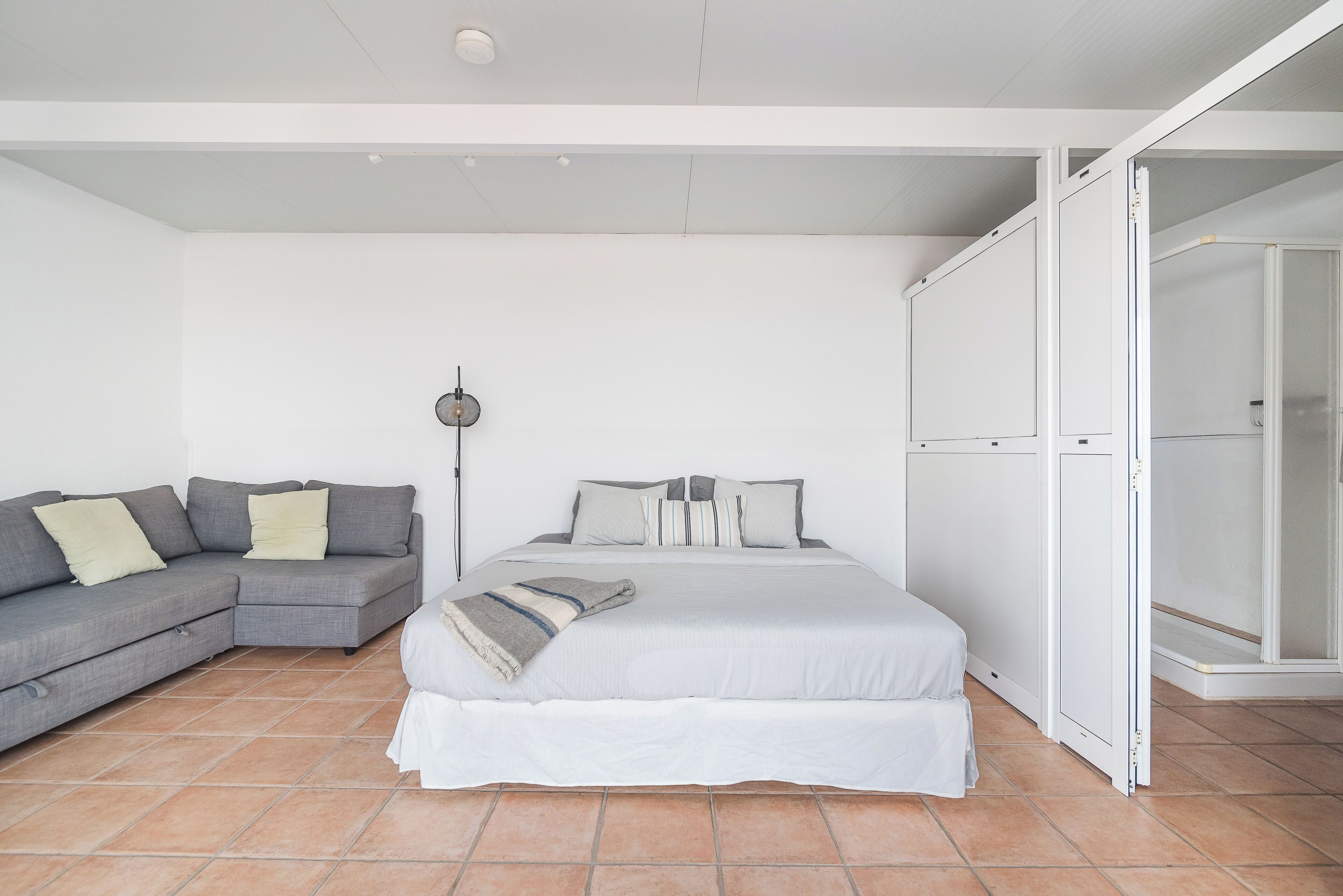 Un dormitorio con cama, sofá gris y vestidor.