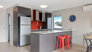 A modern kitchen with a central island, red bar stools, a stainless steel refrigerator, and a clock on the wall.