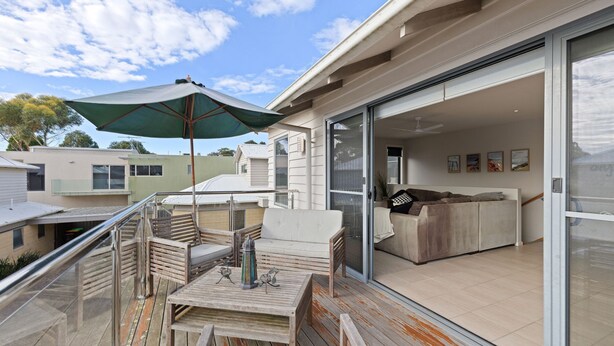 A modern outdoor living area with a wooden deck, a table, and a green umbrella.