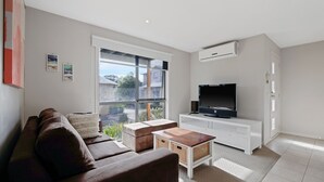 A modern living room with a sofa, a coffee table, and a TV on a white cabinet.