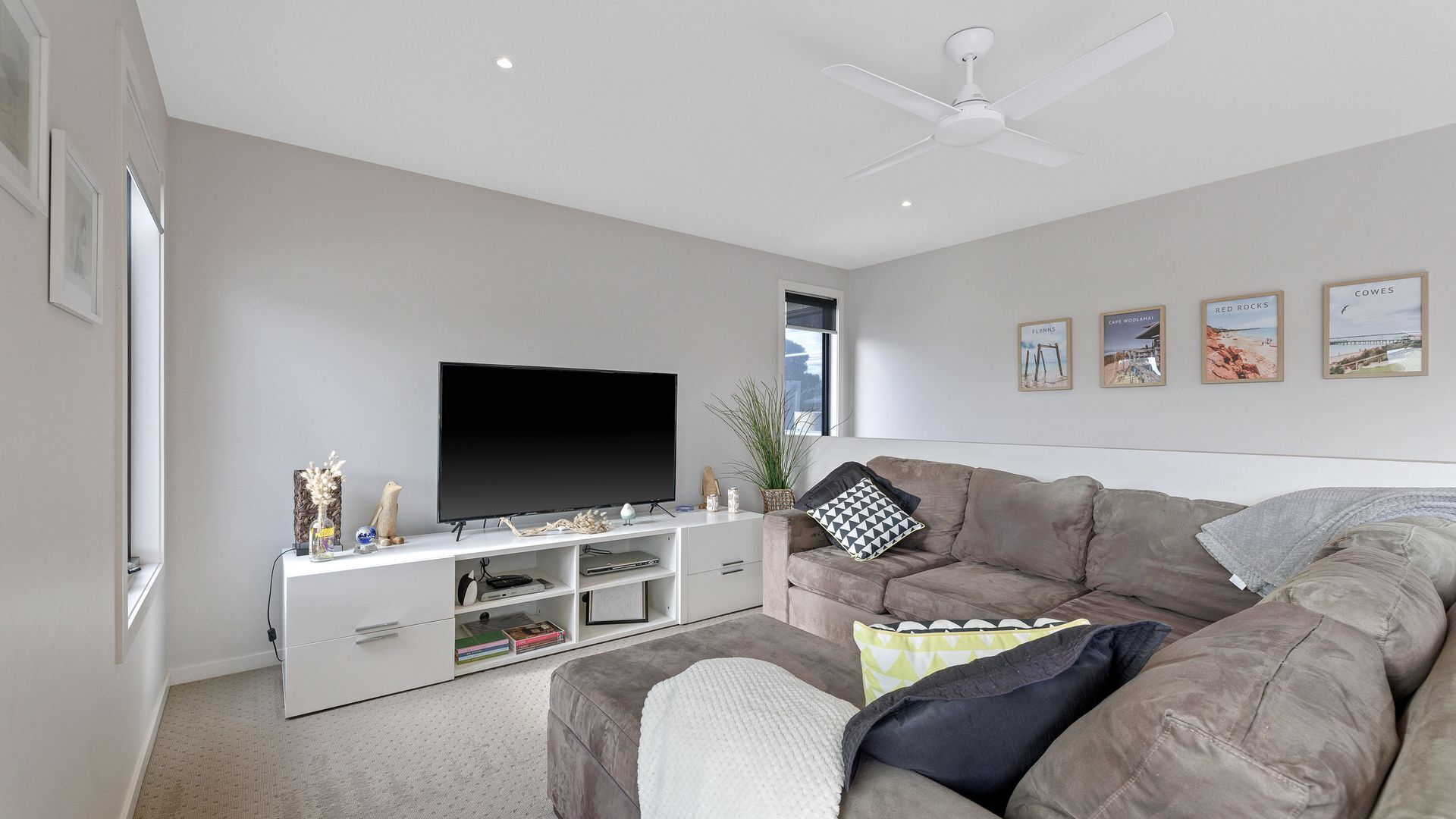 A modern living room with a flat-screen TV, a ceiling fan, and a sofa with decorative pillows.