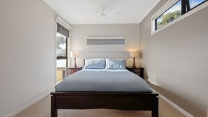 A bedroom with a bed, two bedside tables, a ceiling fan, a window, and a painting on the wall.