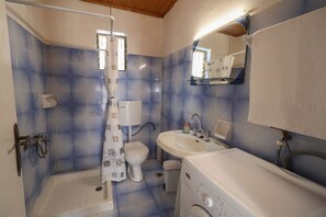 A bathroom with a shower, toilet, sink, and a washing machine.