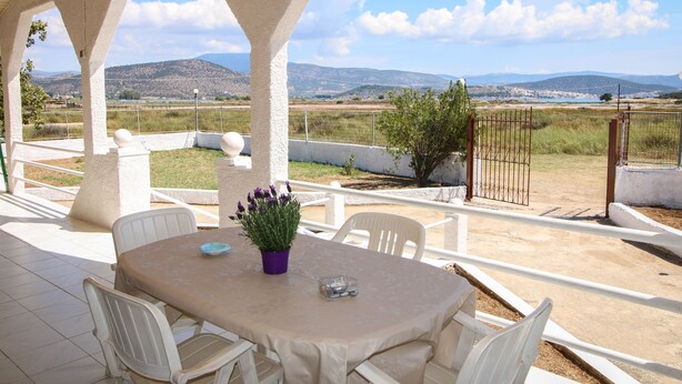 A covered outdoor patio with a table and chairs, a potted plant, and a view of distant hills. - Seaside serenity apartment (Ermionida)