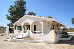 A white building with a red-tiled roof, a covered porch, and a staircase leading to the entrance.