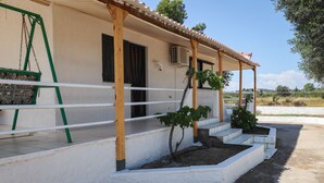 A building with a covered porch, a swing set, and a small garden area. - Seaside serenity apartment (Ermionida)