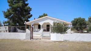 A small, single-story building with a white exterior and a red roof, surrounded by a white wall and a metal fence. - Seaside serenity apartment (Ermionida)