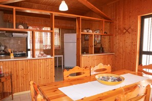 A wooden cabin interior with a kitchen, dining area, and a large window.