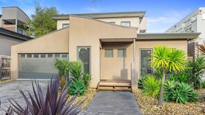 Ein modernes, zweistöckiges Haus mit Garage, einer kleinen Veranda und verschiedenen tropischen Pflanzen.