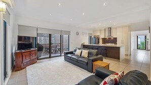 A spacious living area with a sofa, a TV, and a kitchen in the background. - Cowes Central Getaway (Cowes)