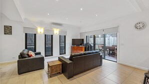A modern living room with a large sofa, a TV, and a dining area with a table and chairs. - Cowes Central Getaway (Cowes)