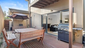 An outdoor patio with a wooden table and chairs, a barbecue grill, and a sliding glass door leading to an indoor living area. - Cowes Central Getaway (Cowes)