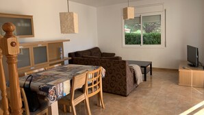 Una sala de estar con una mesa de comedor, dos sofás, un televisor y una ventana con vistas a zonas verdes.