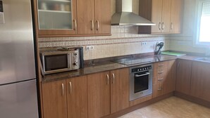 Una cocina con armarios de madera, un refrigerador de acero inoxidable, un microondas, una estufa y una ventana con persianas.