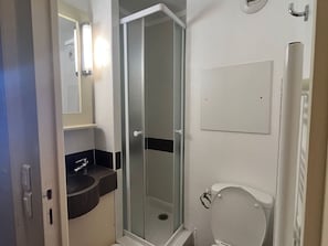 Ein Badezimmer mit einer Duschkabine, Toilette, Waschbecken mit dunkler Arbeitsplatte und Spiegel.
