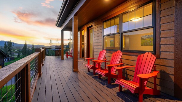 Um deck de madeira com cadeiras Adirondack vermelhas e vista para as montanhas.