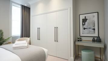 A modern bedroom with a large bed, a desk with a chair, a wardrobe, and a framed abstract painting on the wall.