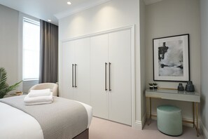 A modern bedroom with a large bed, a desk with a chair, a wardrobe, and a framed abstract painting on the wall.