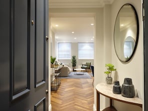 A modern living room with a herringbone floor, a round table with vases, and a large mirror on the wall.