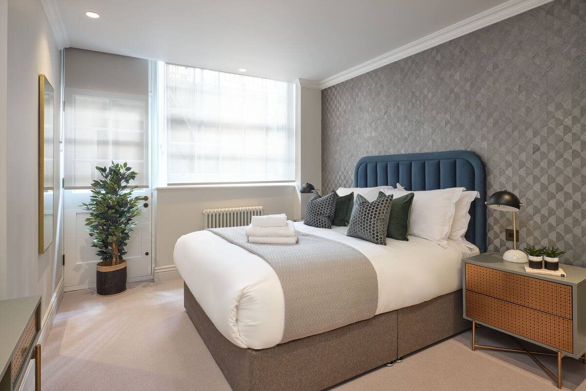 A modern bedroom with a large bed, a bedside table with a lamp, and a potted plant.