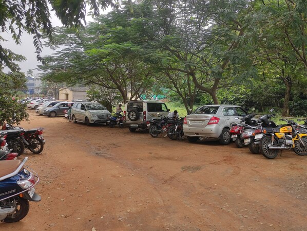 Un espace de stationnement où sont garées de nombreuses voitures et motos, entouré d’arbres.