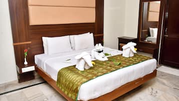 Habitación de hotel con una cama grande, cabecero de madera, mesita de noche con un jarrón de flores y un espejo en la pared.