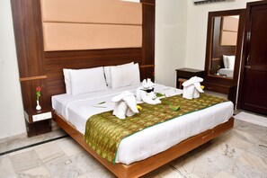 A hotel room with a large bed, wooden headboard, a nightstand with a vase of flowers, and a mirror on the wall. - SET RESIDENCY (Kumbakonam)