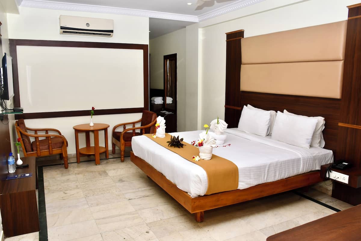 A hotel room with a large bed, a desk, two chairs, a small table, and a mirror.