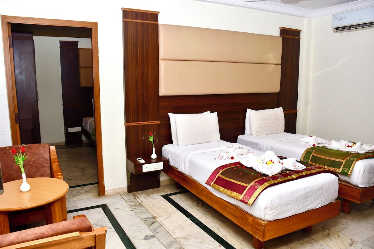 A hotel room with two beds, a wooden headboard, a small table with a vase, and a chair.