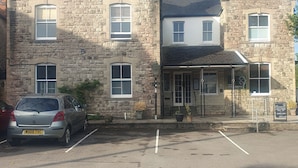 A stone building with multiple windows, a car parked in front, and a sign indicating a restaurant. - The Shrubbery Hotel (Shepton Mallet)