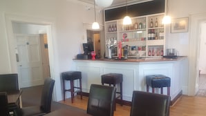 A bar area with stools, a counter, and a variety of bottles. - The Shrubbery Hotel (Shepton Mallet)