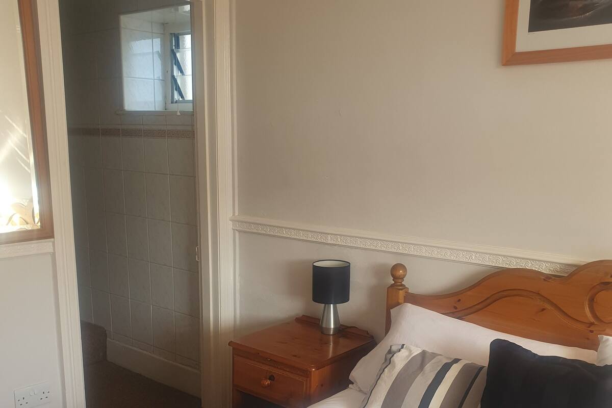 Quarto com cama, mesa de cabeceira, luminária e quadro na parede.